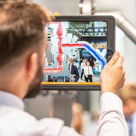 LEWA-orange-showroom-employee-holding-tablet-showing-remote-head-animation-AR-trade-fair-achema-1.jpg