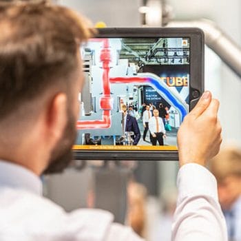 LEWA-orange-showroom-employee-holding-tablet-showing-remote-head-animation-AR-trade-fair-achema